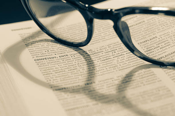 Close up of an open dictionary with glasses under the word "comp?tant", in french, which means "competent"
